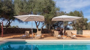 A swimming pool with lounge chairs and umbrellas, surrounded by trees and a stone wall. - Finca Son Grauet - Spectacular villa with pool in Llucmajor (LLucmajor)