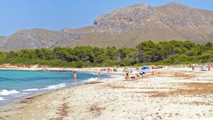 Ein Strand mit klarem türkisblauem Wasser, einem sandigen Ufer und einem Bergpanorama im Hintergrund.