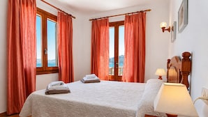 Ein Schlafzimmer mit einem Bett, einem Nachttisch, einer Lampe und einem Fenster mit Vorhängen.