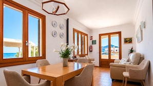 Ein Essbereich mit Holztisch und Stühlen, einem Blumentopf und Blick auf das Meer durch große Fenster.