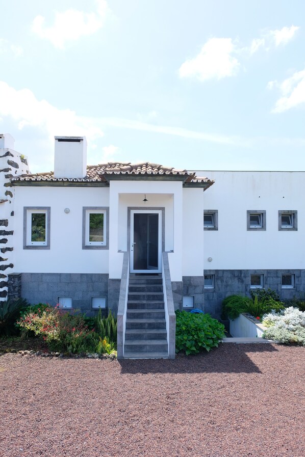 Una casa moderna con fachada blanca, techo de tejas y una escalera central que conduce a la entrada.