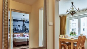 A bedroom with a large mirror reflecting a cityscape, a wooden dining table with chairs, and a chandelier. - Irena and Anatol Apartment - 5 min walk to Krakow’s Main Square! Sleeps 4!  (Kraków)