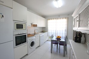 Een moderne keuken met witte kastjes, een inbouwoven, magnetron en wasmachine.