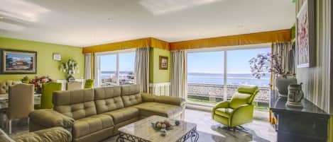 Un salon comprenant un canapé, des fauteuils, une table basse et offrant une vue sur la mer grâce à de grandes fenêtres.