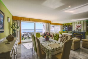 A dining area with a table set for four, a sofa, and a view of the sea. - 1149 Stunning Duplex Penthouse with Panoramic Sea Views (Marbella)