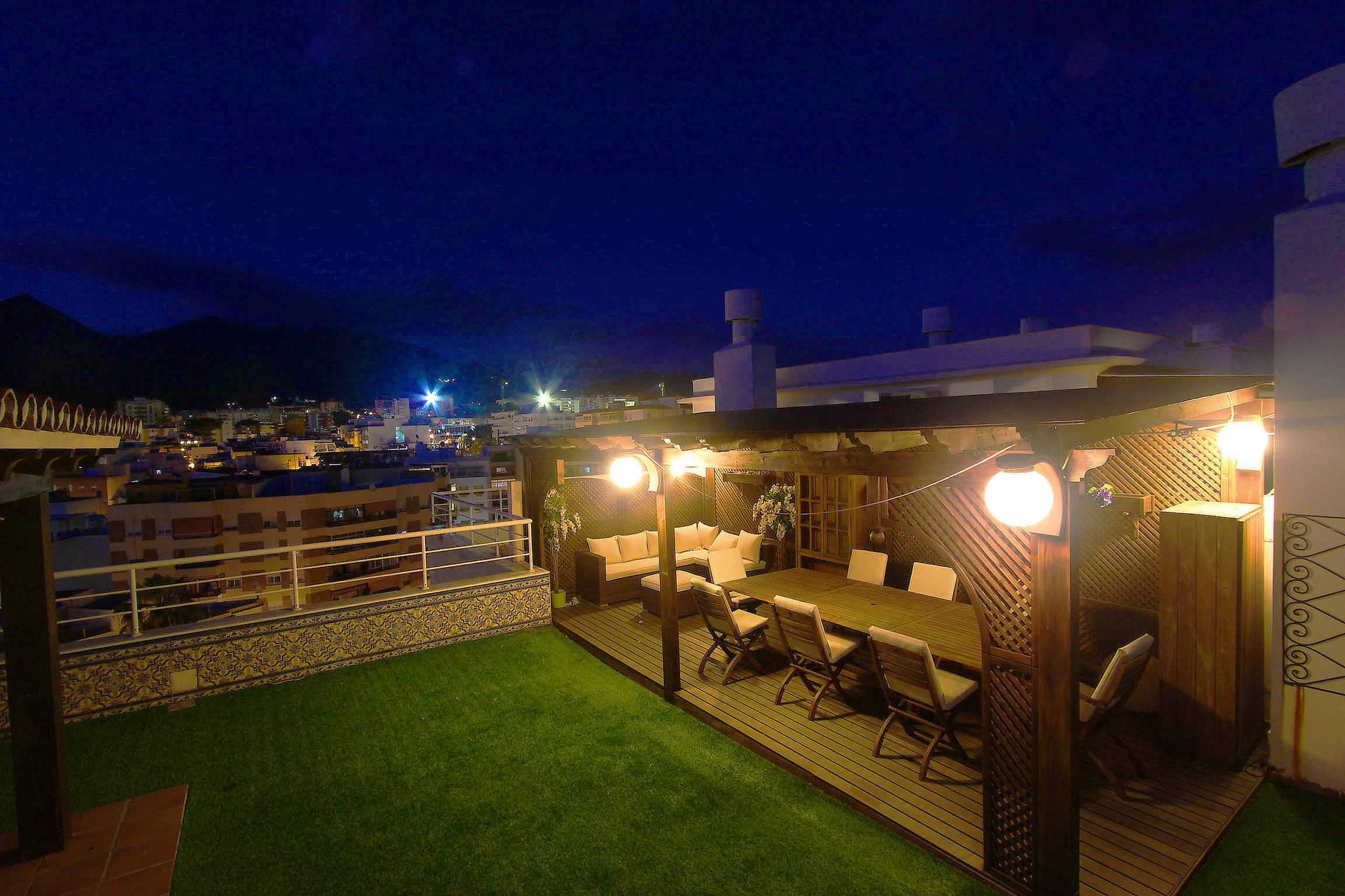 Une terrasse sur le toit avec une plateforme en bois, du mobilier d’extérieur et des guirlandes lumineuses.