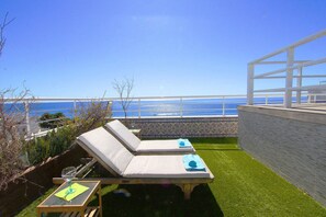 Een dakterras met twee loungesteilen, een tafel met een glas en uitzicht op de oceaan.