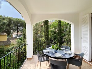 A balcony with a table set for dining, surrounded by chairs, and overlooking a garden with trees and a building in the background. - Holiday rental apartment in Begur, Sa Riera (Begur)