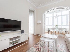 A modern living room with a flat-screen TV, white entertainment unit, and a dining area with a table and chairs. - ART HOUSE VILADOMAT APARTMENT (BARCELONA)
