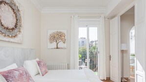 A bedroom with a large bed, a radiator, a window with curtains, and a view of the outside balcony.