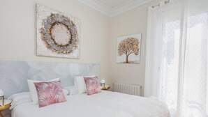 A bedroom with a large bed, two wall-mounted artworks, a radiator, and sheer curtains.