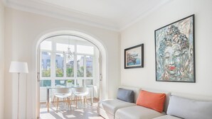 A modern living room with a sofa, a dining table with chairs, and a large window.