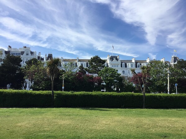 A large, white building with multiple chimneys and a flag, surrounded by well-maintained hedges and trees.