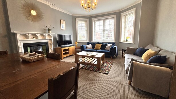 A living room with a fireplace, television, sofa, and dining table. - Silverdale Sunbeams, 4 bedroom spacious apartment close to seafront (Eastbourne)