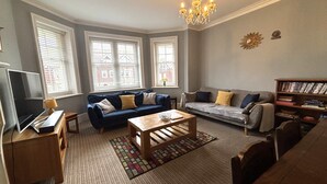 A living room with a sofa, a coffee table, a TV, and a bookshelf. - Silverdale Sunbeams, 4 bedroom spacious apartment close to seafront (Eastbourne)
