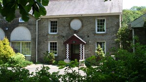 A stone building with a central entrance, multiple windows, and a surrounding garden. - Family friendly coachhouse in idyllic setting with extensive private grounds and free WiFi (Swansea)