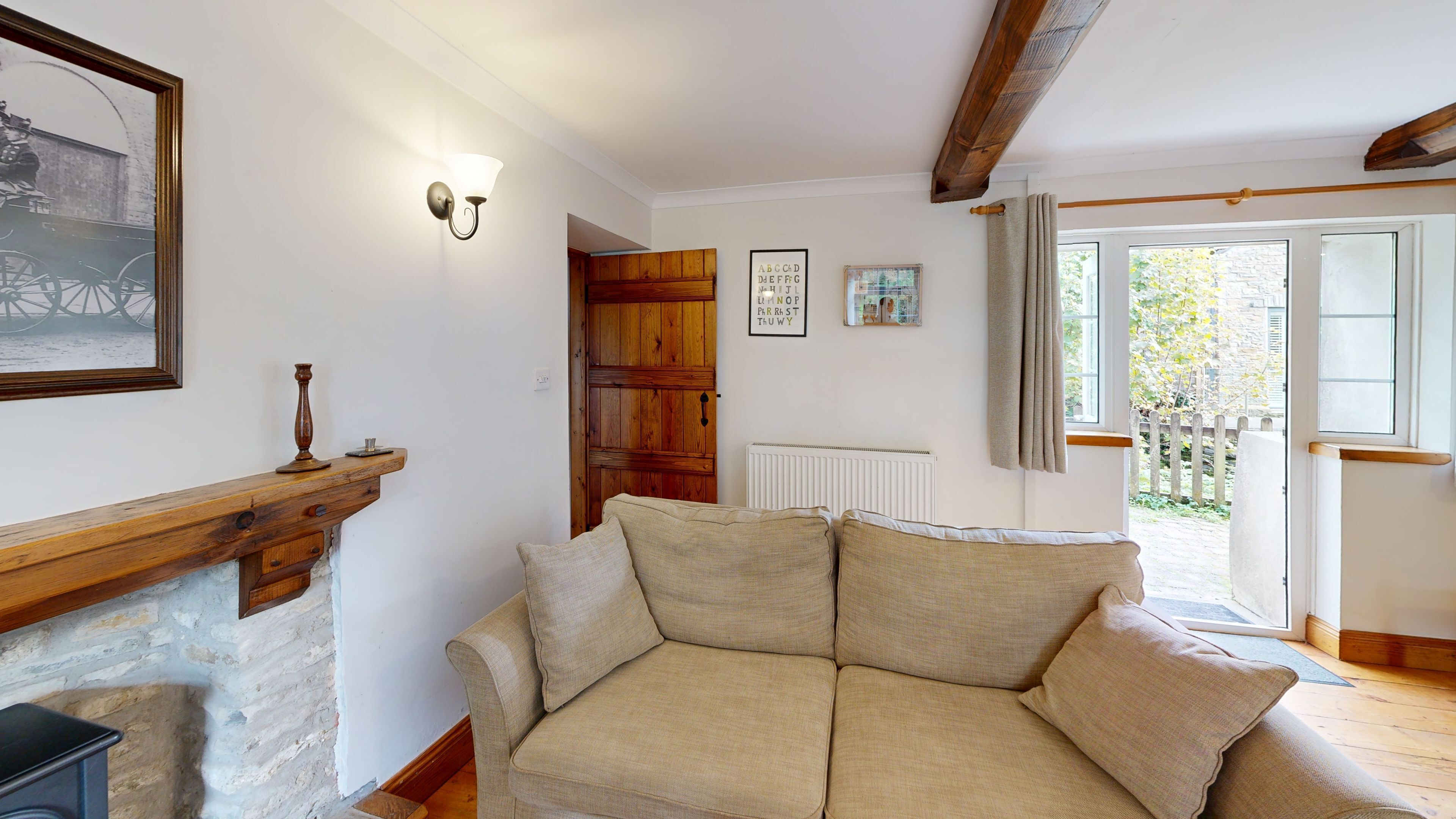 Ein gemütliches Wohnzimmer mit einem beigen Sofa, einem hölzernen Kaminvorsatz, einer wandmontierten Leuchte und einer Tür, die nach draußen führt.
