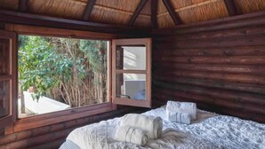 Ein Holzhüttenraum mit Bett, Fenster und Blick auf Bäume.