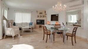Ein geräumiges Wohnzimmer mit einem Glastisch, weißen Sofas, einem Fernseher und einer Chandelüster.