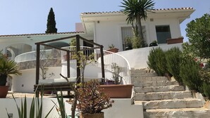 Ein weißes Gebäude mit einer Steintreppe, Blumentöpfen und einer Pergola.