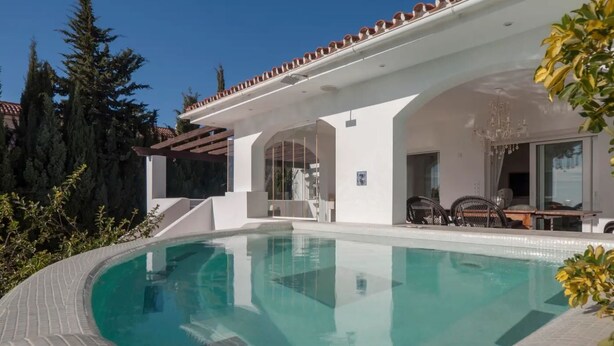 Ein modernes Haus mit Swimmingpool, Sitzgelegenheiten im Freien und einer Pergola.