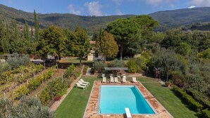 Ein rechteckiger Swimmingpool mit einer gefliesten Liegefläche, umgeben von einem gepflegten Rasen und mehreren Liegestühlen.