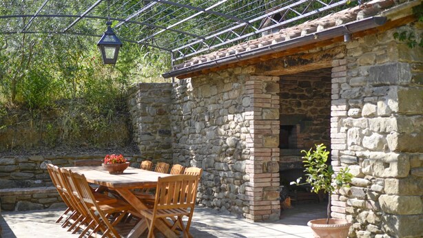 Ein Steinhaus mit Ziegeldach, einem Holztisch mit Stühlen und einem Blumentopf.