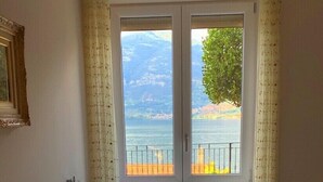 Une chambre à coucher avec un lit, deux oreillers, une fenêtre donnant sur une plage et des montagnes, et un rideau.