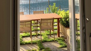 Un balcon avec une table et des chaises, donnant sur un lac avec des montagnes en arrière-plan.