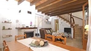 A dining area with a wooden table, chairs, and a decorative centerpiece. A staircase leads to another room with a television and a sofa. - Victori - Charming country house with pool in Sineu, Mallorca (Sineu)