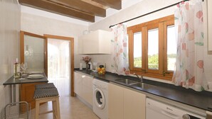 A compact kitchen with a washing machine, a dishwasher, a sink, and a dining area with a table and chairs. - Victori - Charming country house with pool in Sineu, Mallorca (Sineu)