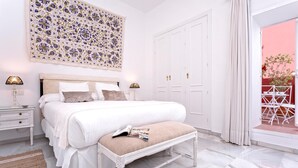 Un dormitorio con una cama grande, mesitas de noche, un banco, un adorno en la pared y vistas a una pared roja y un balcón.