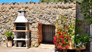 Un bâtiment en pierre doté d’une entrée rustique, d’un petit four extérieur et de plantes en pot ornées de fleurs.