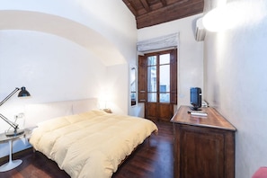 A bedroom with a bed, a desk, a lamp, a TV, and a window with a view.