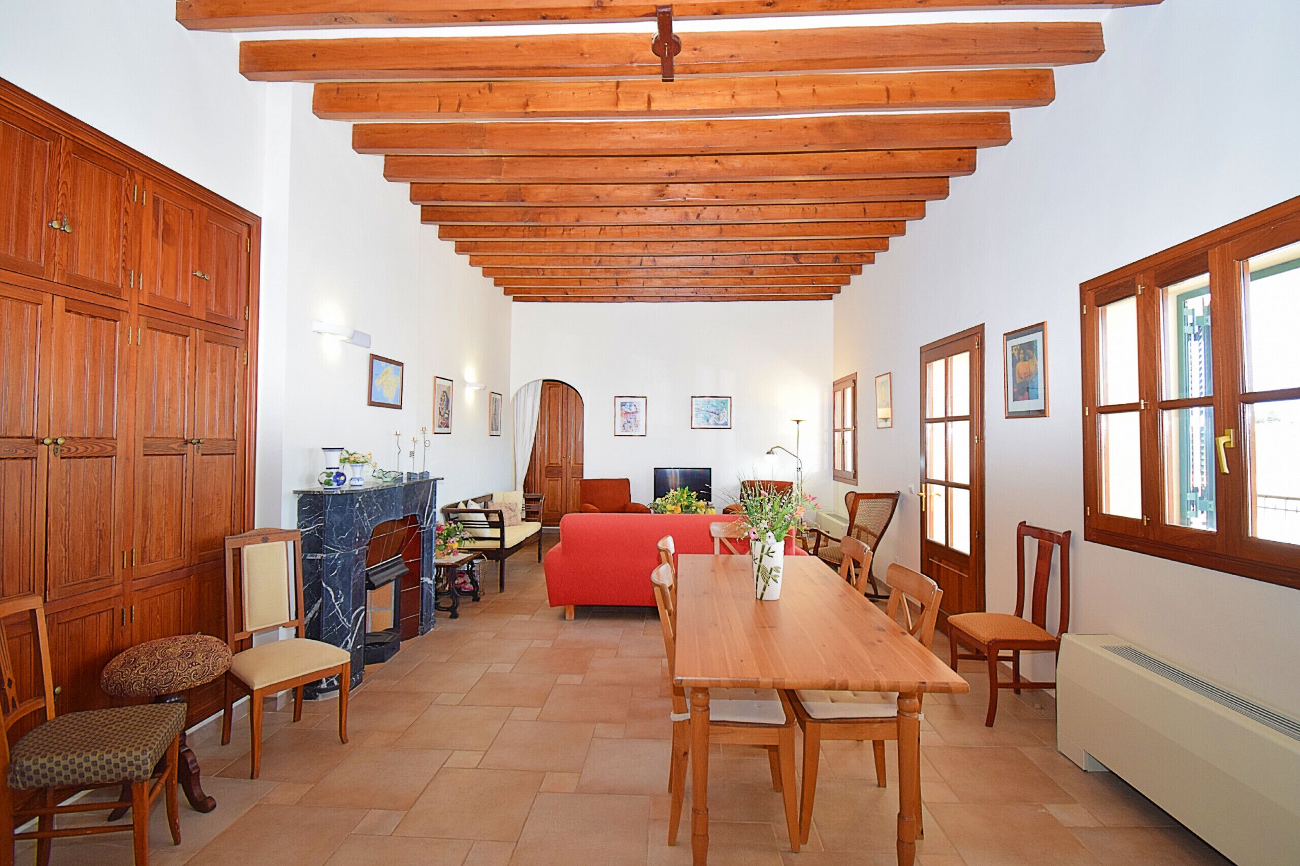 A spacious living area with a wooden dining table, chairs, a red sofa, and a fireplace.