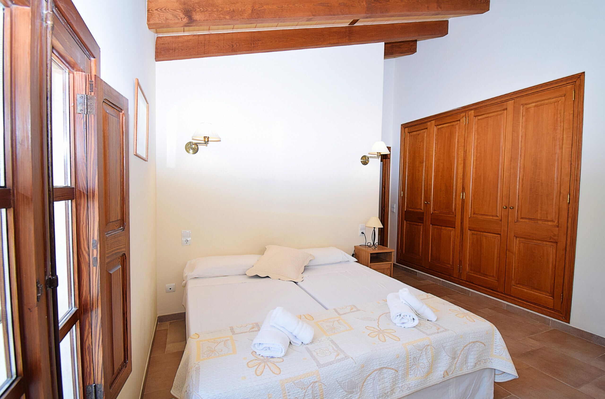 Un dormitorio con cama, armario de madera y mesita de noche con lámpara.