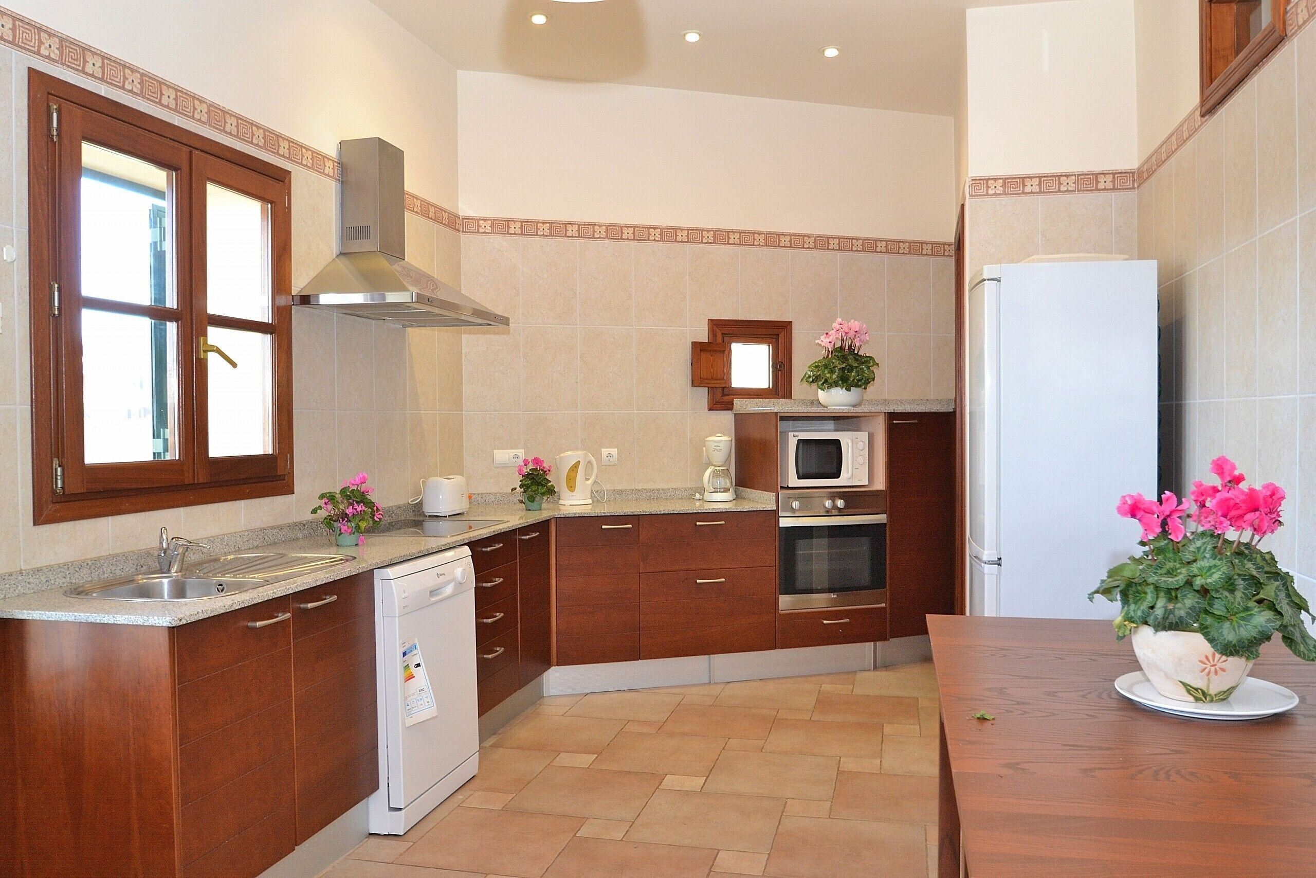 A kitchen with wooden cabinets, a stainless steel range hood, a built-in microwave, and a refrigerator.
