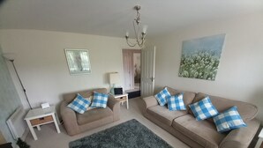 A living room with two beige sofas, a green rug, a white side table, a lamp, and a painting on the wall. - BEAUTIFUL  BRIGHT MODERN GROUND FLOOR APARTMENT,PARKING, WIFI. (Buckshaw Village)