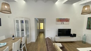 A modern living room with a brown sofa, a dining table with chairs, a TV on a white cabinet, and a glass cabinet with glassware. - Son Coves Rural Cottage (Santanyi)