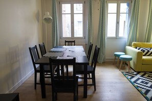 A dining area with a table and chairs, a lamp, a window with curtains, and a yellow sofa. - 22nd - Plein center Honfleur (Honfleur)