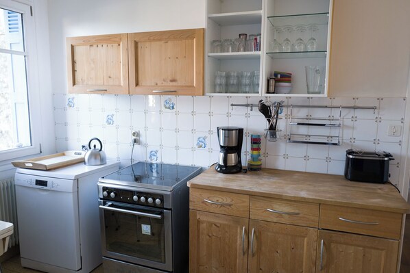 A kitchen with wooden cabinets, a stainless steel stove, a coffee maker, and a tiled backsplash.