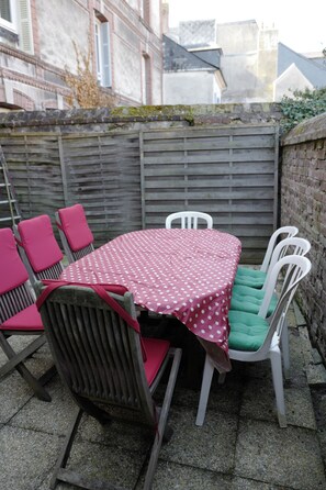 An outdoor patio with a round table, six chairs, and a brick wall. - 22nd - Plein center Honfleur (Honfleur)