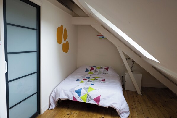 A small bedroom with a sloped ceiling, a bed with a colorful quilt, and a wall with a geometric pattern.