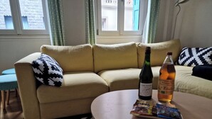 Ein Wohnzimmer mit einem beigen Sofa, einem runden Couchtisch, einer Weinflasche und einer Flasche Spirituosen.