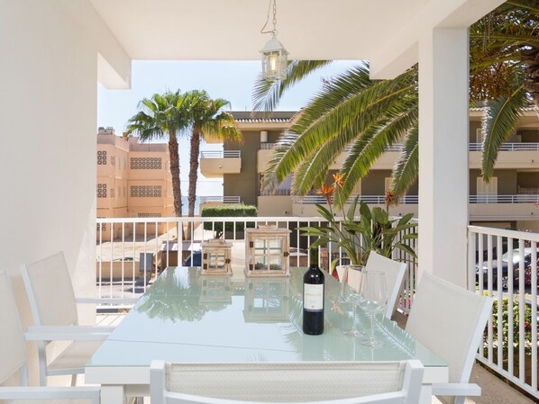 A balcony with a glass table, chairs, a bottle of wine, and a hanging light fixture.