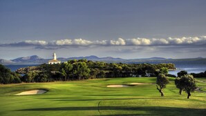 Un campo de golf con búnkeres, un faro y montañas al fondo.