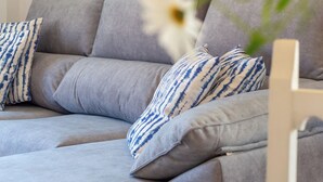 Un sofá seccional gris con almohadones estampados, un jarrón blanco con flores y tres cuadros abstractos en la pared.