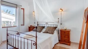 Un dormitorio con cama, mesitas de noche, cómoda de madera, ventana con cortinas y mosquitero.