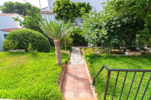 Un chemin de jardin qui mène à un bâtiment blanc doté d’un toit recouvert de tuiles.