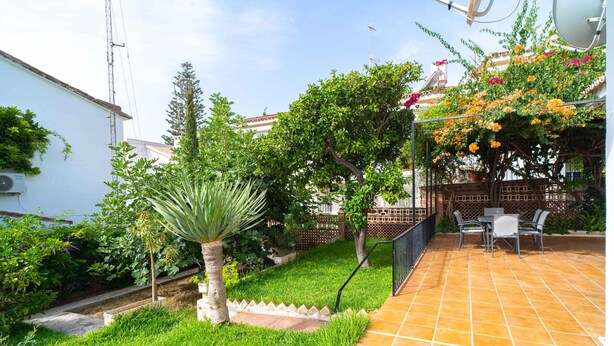 Une terrasse avec un sol carrelé, un petit jardin avec de la pelouse et des plantes, et un mur en briques.